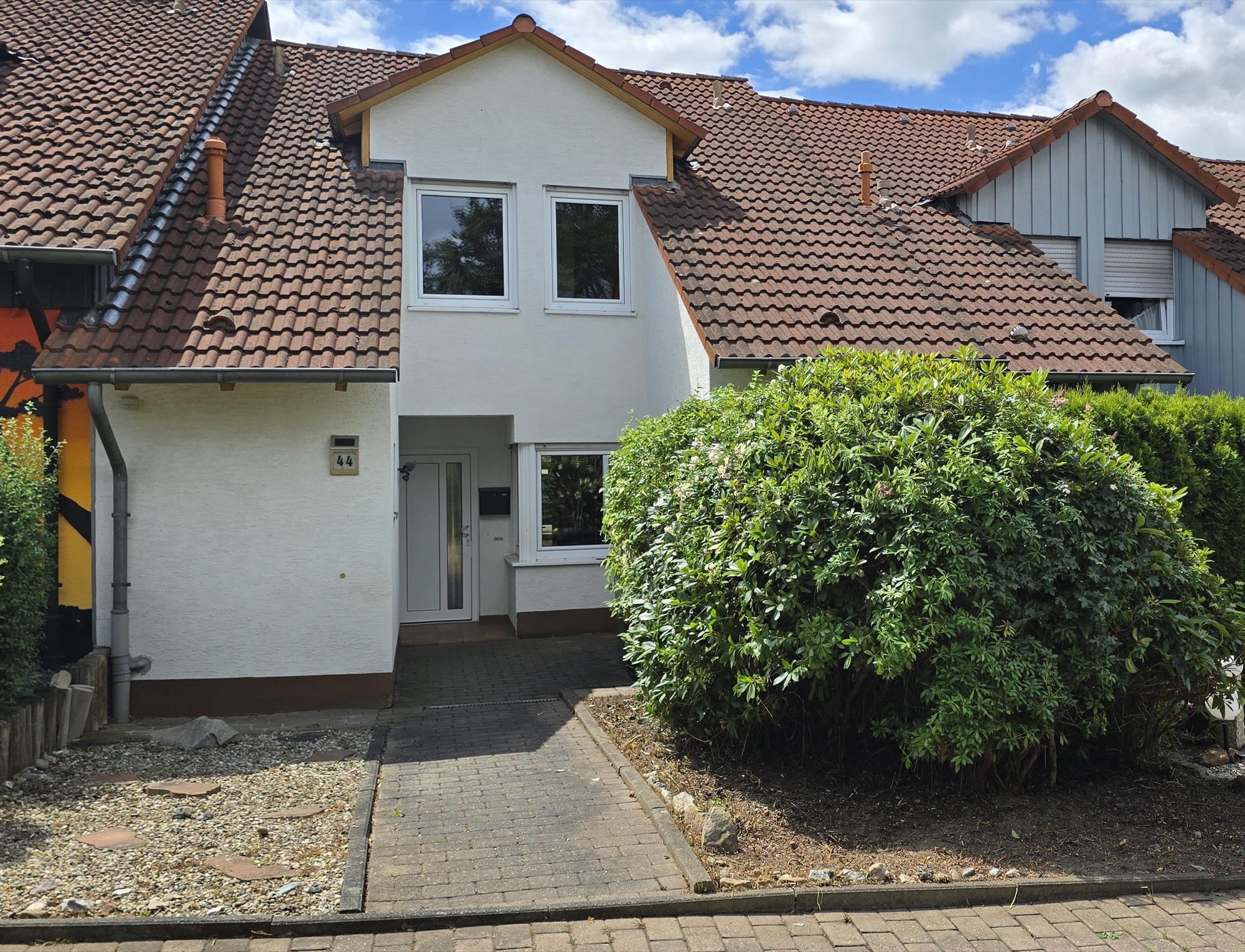 Straßenansicht des Reihenmittelhauses mit weißer Fassade und rotem Ziegeldach